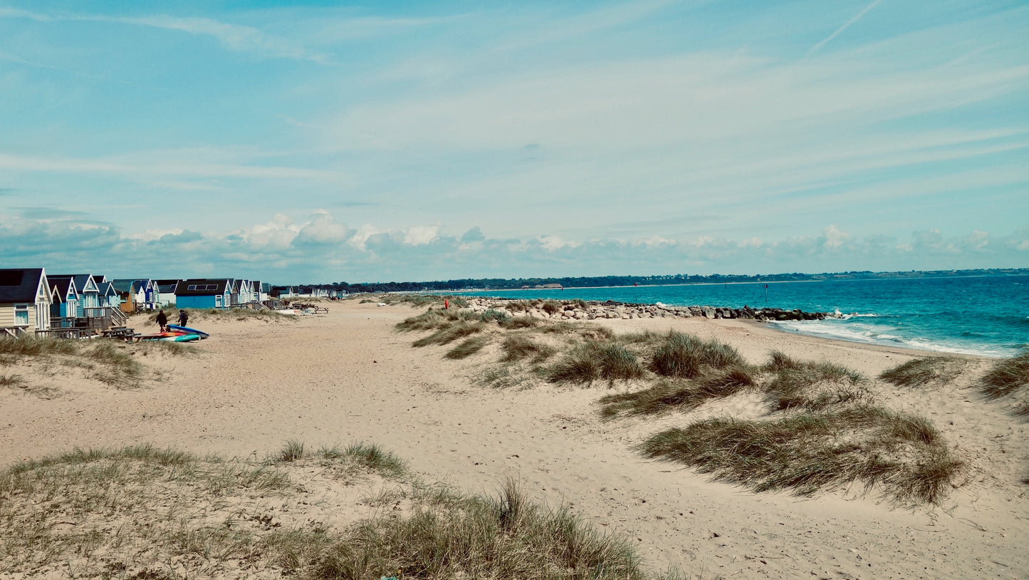 View along Hengistbury Head beach, beach huts and dunes with the shore line of Museford and Highcliffe off in the distance